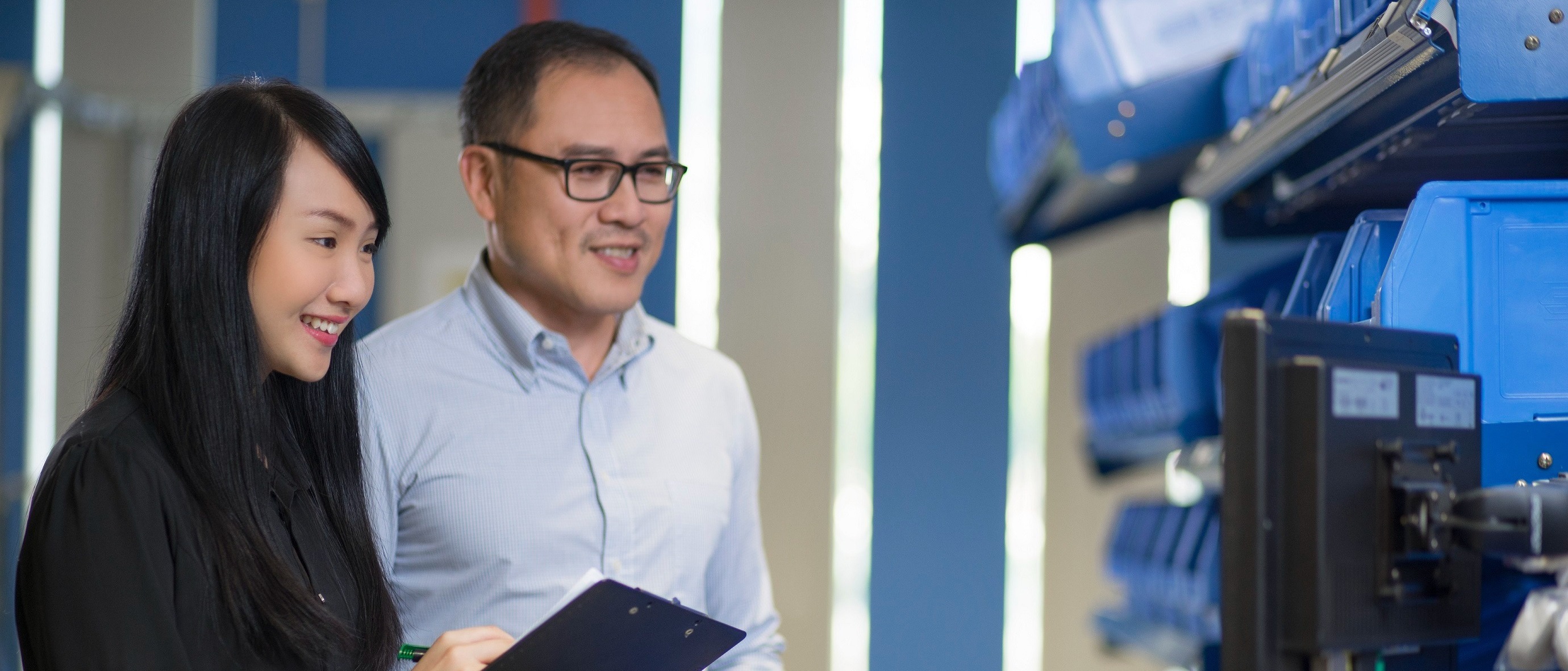Two people smile while standing in an office, observing a monitor. 